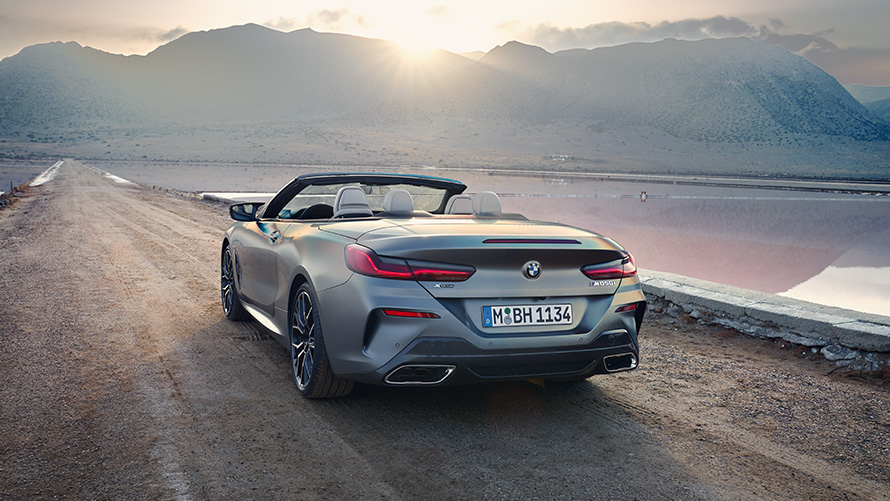 BMW 8 Series Convertible G14 LCI Facelift 2022 BMW Individual Frozen Pure Grey metallic rear view with open softtop standing on sandy road with hills in the background
