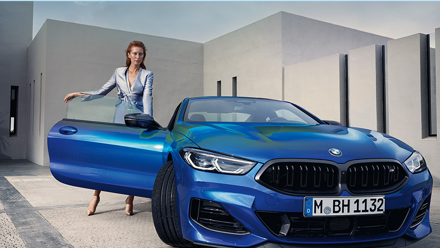 BMW M850i xDrive Coupé G15 LCI Facelift 2022 M Portimao Blue metallic front view standing with female model in open front door