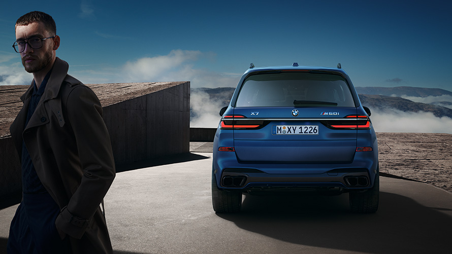 BMW X7 M60i xDrive G07 LCI Frozen Marina Bay Blue rear view standing in front of mountain landscape with model